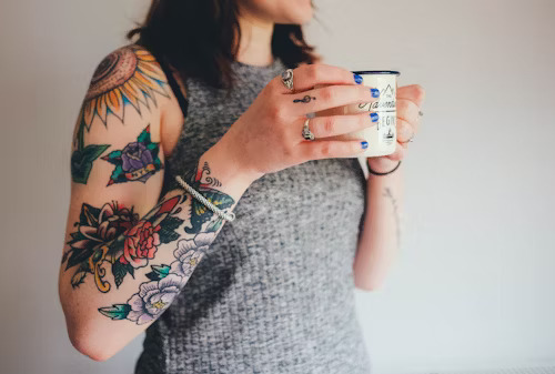 A bottle of sunscreen sits next to a colorful tattoo, showing why it's important to protect new tattoos from the sun.